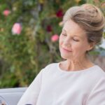 Kobieta 50+ czyta książkę na świeżym powietrzu. W tle kwiaty.